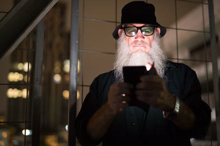 Mature bearded man looking suspicious while using phone