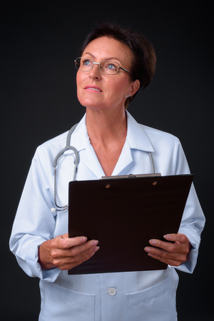 Mature beautiful woman doctor with short hair against black backの写真素材