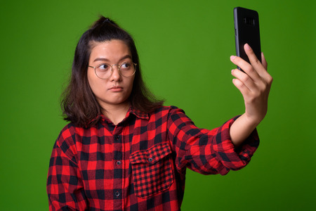 Young beautiful Asian hipster woman wearing eyeglasses and red checkered shirtの写真素材