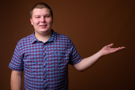 Studio shot of overweight young man against brown backgroundの写真素材