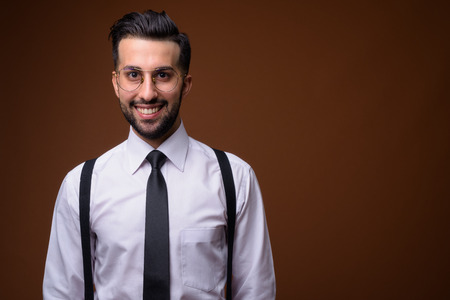 Young handsome bearded Iranian businessman against brown backgroの写真素材