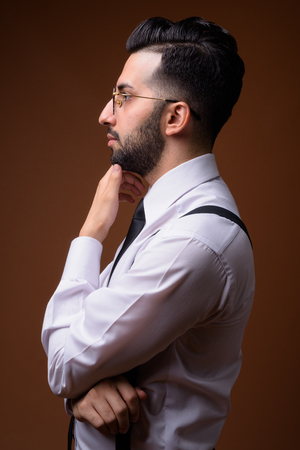 Young handsome bearded Iranian businessman against brown backgroの写真素材
