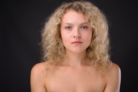 Young beautiful woman with blond curly hair against gray backgroの写真素材