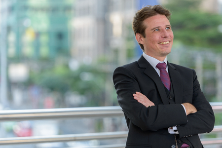 Happy businessman smiling and thinking with arms crossed on footの写真素材