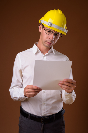 Portrait of businessman wearing hardhat against brown backgroundの写真素材