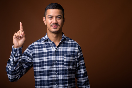Young multi-ethnic Asian man against brown backgroundの写真素材