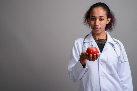 Young beautiful African woman doctor against gray backgroundの写真素材