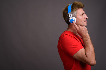 Man with blond hair listening to music against gray backgroundの写真素材