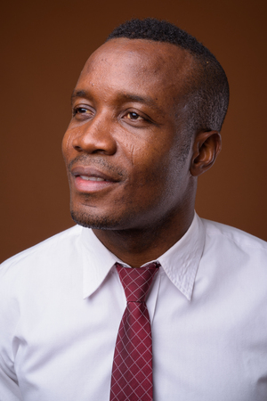 Studio shot of young African businessman against brown backgrounの写真素材