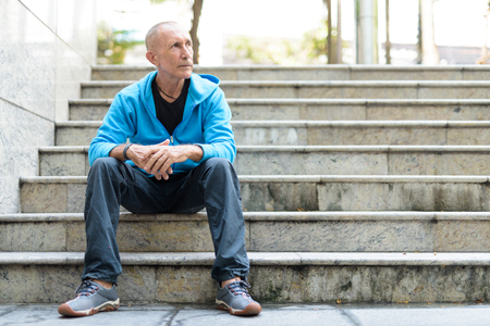 Full body shot of bald senior man thinking while sitting on theの写真素材