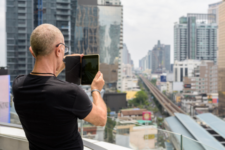 Back view of bald senior tourist man taking picture with digitalの写真素材