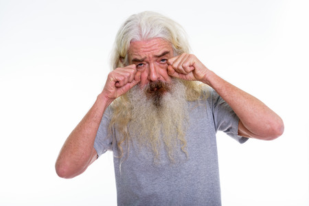 Studio shot of senior bearded man looking sad while crying with