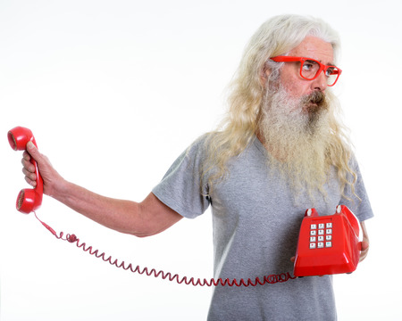 Studio shot of senior bearded man holding old telephone while loの写真素材