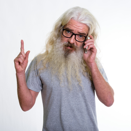 Studio shot of senior bearded man talking on mobile phone and po