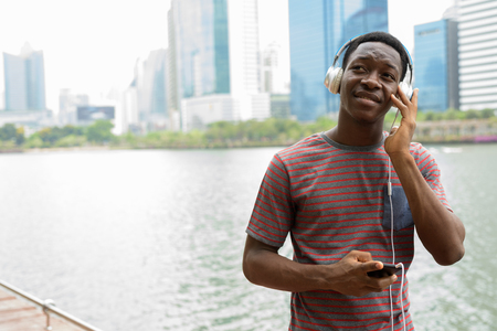 Happy African man in park using mobile phone and listening music with headphonesの写真素材