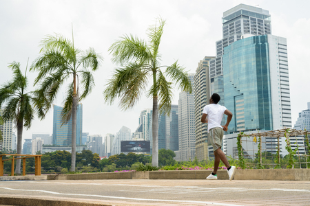 Young African man running outdoors in park with cityscapeの写真素材