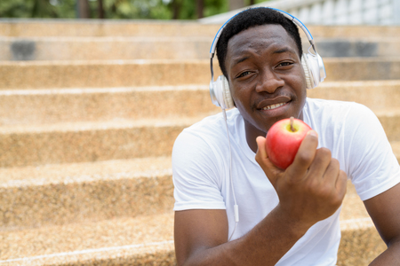 African man listening music with headphones and holding red appleの写真素材