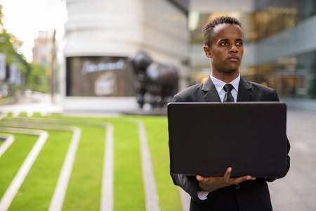 African businessman using laptop computer while thinking outdoorsの写真素材