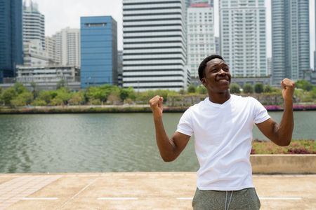 Young handsome African man with arms raised outdoors with cityscape backgroundの写真素材