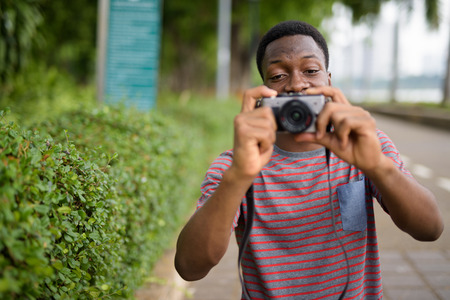 Young handsome African man taking pictures with camera in parkの写真素材