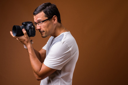 Portrait of photographer man taking picture against brown backgroundの写真素材