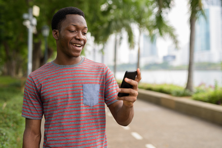 Young handsome African man using mobile phone in parkの写真素材