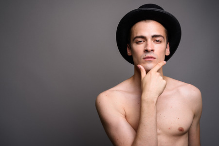 Portrait of shirtless man wearing hat against gray studio backgroundの写真素材