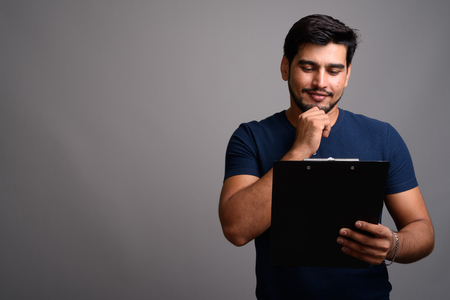 Young handsome bearded Persian man against gray backgroundの写真素材
