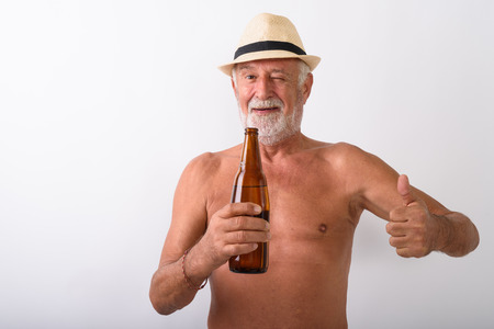 Shirtless senior man holding beer bottle against white backgroundの写真素材