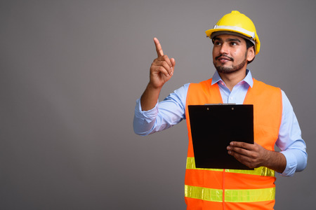 Young handsome bearded Persian man construction worker against g