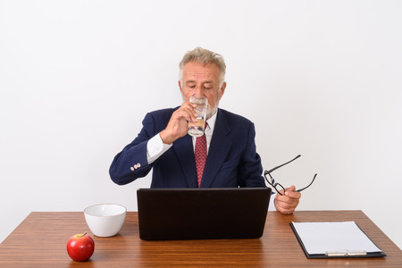 Studio shot of handsome senior bearded businessman holding eyeglの写真素材