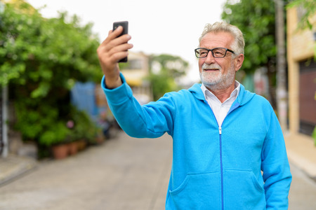 Happy handsome senior bearded man smiling while taking selfie piの写真素材