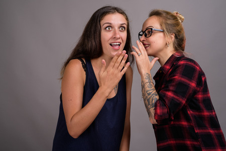 Two young beautiful woman gossip against gray background