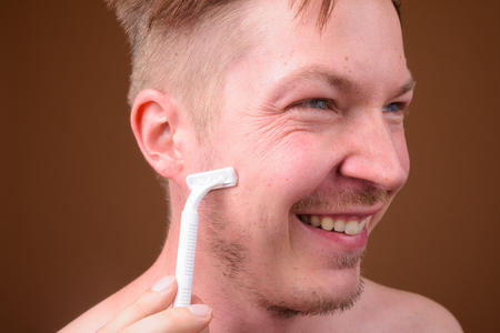 Face of shirtless man shaving using razorの写真素材