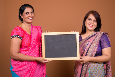 Two happy Indian woman holding empty black board with copy spaceの写真素材