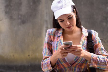 Young beautiful Asian woman using mobile phone outdoors