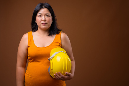 Overweight Asian woman construction worker holding hardhatの写真素材