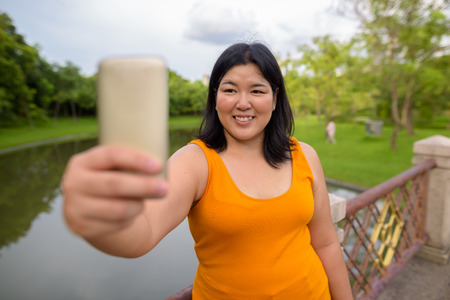 Beautiful overweight Asian woman taking selfie in parkの写真素材