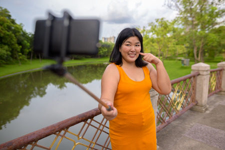 Asian woman taking selfie with mobile phone attach to selfie stick in park