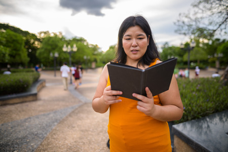 Beautiful overweight Asian woman reading book in parkの写真素材