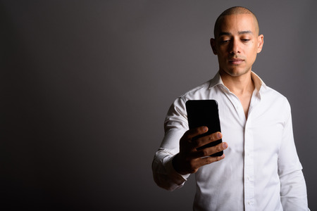 Handsome bald businessman using mobile phone against gray backgrの写真素材