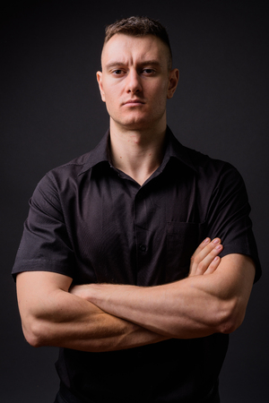 Young handsome businessman with arms crossed against gray backgroundの写真素材