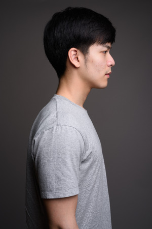 Profile view of young handsome Asian man against gray backgroundの写真素材