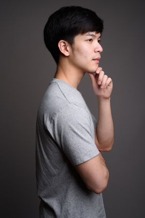 Profile view of young handsome Asian man thinkingの写真素材