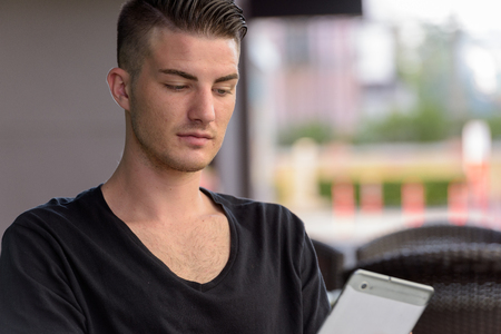 Young man using digital tablet outdoors while sittingの写真素材
