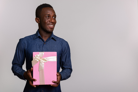 Young happy African man smiling and holding gift box while thinkの写真素材