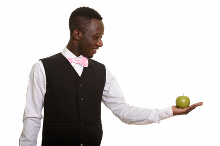 Young happy African waiter smiling and holding green appleの写真素材