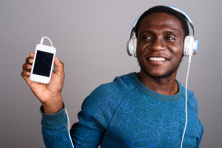 Young African man listening to music against gray backgroundの写真素材