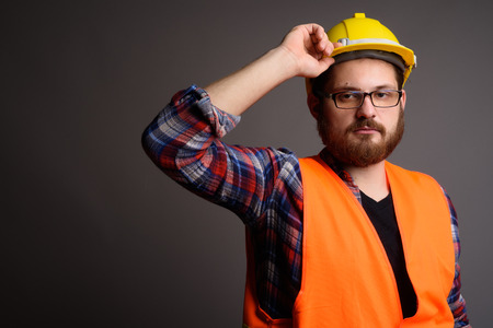 Young bearded man construction worker against gray background