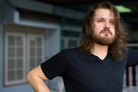 Young bearded man with long hair thinking at home outdoorsの写真素材